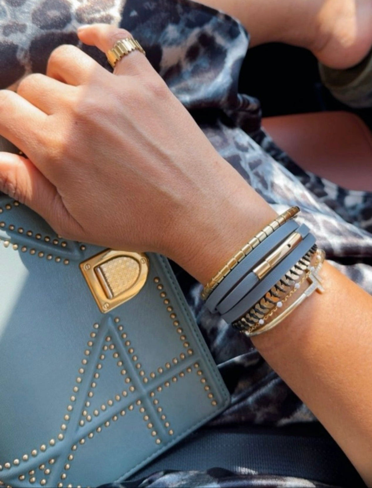 Hand holding a blue clutch with gold accents, wearing a gold bracelet and ring.